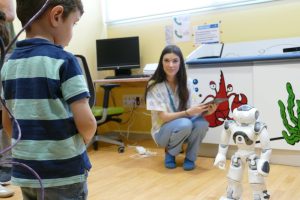 En la imagen una terapeuta está junto a Juande, un robot tipo Nao que apoya en las terapias de niños con dificultades neuromotoras