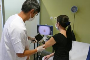 En la imagen un doctor explora el lunar de una paciente que está sentada en una camilla