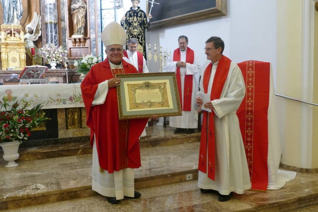 En la imagen dos señores se sitúan en el altar de una Iglesia mientras uno entrega a otro un cuadro